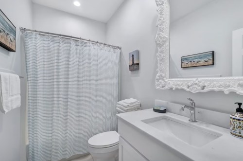 Bright bathroom featuring a white vanity, a shower curtain, and decorative coastal artwork on the walls.