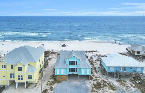 Aerial view of colorful beach houses near a sandy shore and ocean waves under a blue sky.