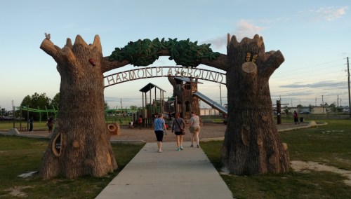 Entrance to Harmon Playground featuring large tree sculptures and playground equipment in the background.