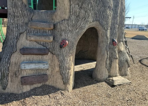 A textured play structure resembling a tree, featuring steps, ladybug decorations, and a tunnel entrance.