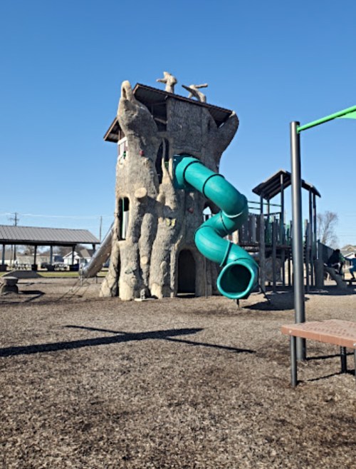 Playground featuring a treehouse structure with a green slide and climbing features, set in a sunny outdoor area.