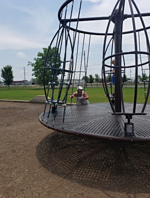 A playground with a large spinning structure; a child is playing on it while another child is visible in the background.
