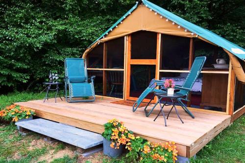 A cozy glamping tent with a wooden deck, chairs, and potted flowers, surrounded by greenery.