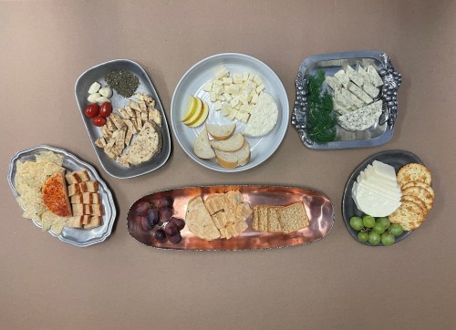 A variety of cheeses, crackers, fruits, and herbs arranged on platters, creating a colorful and inviting spread.
