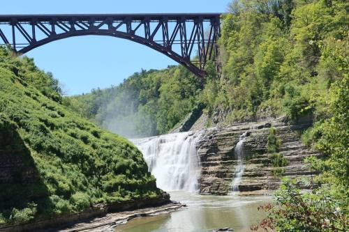 A scenic view of a waterfall surrounded by lush greenery, with a large bridge arching overhead.