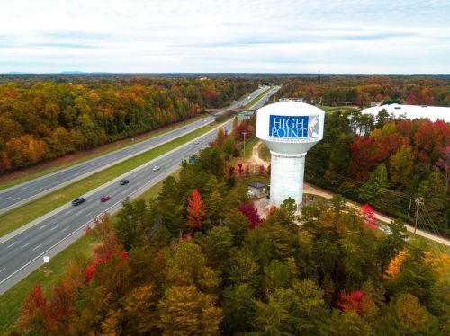 Aerial view of a water tower labeled "High Point" surrounded by colorful autumn trees and a highway.