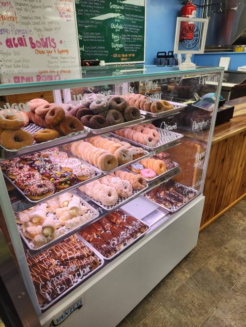 A display case filled with various donuts, including glazed, chocolate, and sprinkled varieties, in a colorful bakery.