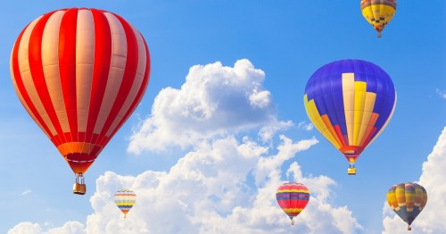 Colorful hot air balloons floating in a bright blue sky with fluffy white clouds.