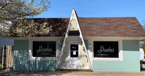 A quaint bakery with a unique triangular roof and large windows, featuring the name "Bunde's Bakery & Cafe" on the facade.