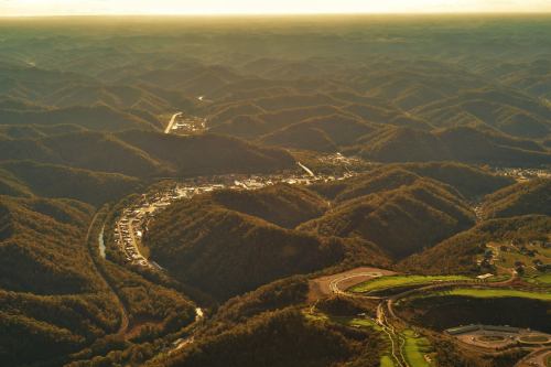 Aerial view of rolling hills and valleys, with a small town nestled among the mountains under a golden sunset.