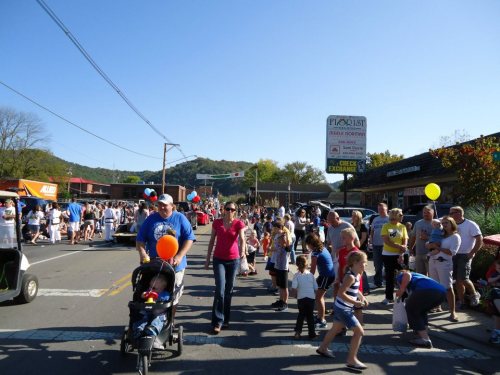 A lively street scene with families and children walking, balloons in hand, during a community event or festival.