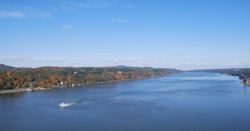 A scenic river view with autumn foliage along the banks and a boat cruising on the water under a clear blue sky.