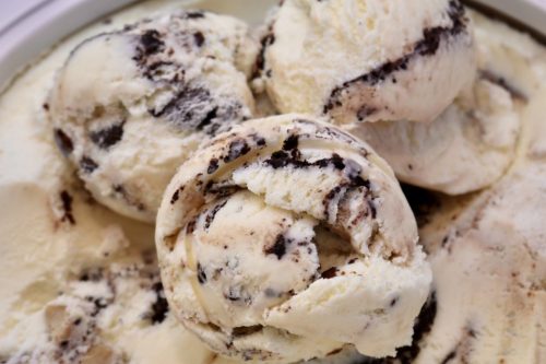 Close-up of creamy vanilla ice cream swirled with chocolate cookie pieces in a bowl.