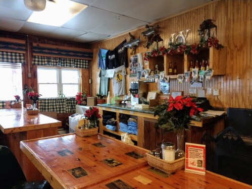 Cozy wooden interior of a restaurant with tables, decorations, and a counter displaying photos and memorabilia.