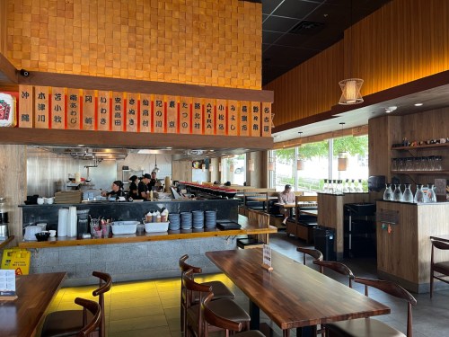 Interior of a restaurant featuring wooden decor, a sushi bar, and a menu displayed on the wall.