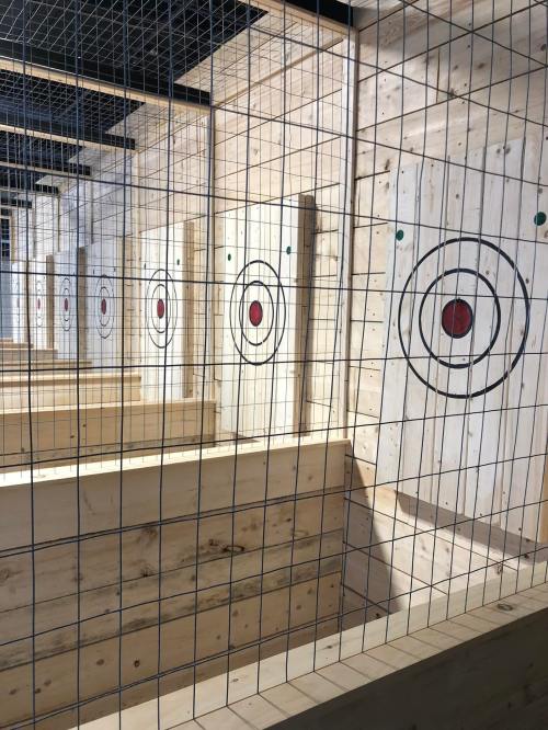 A row of wooden targets with red bullseyes, enclosed in a wire mesh structure, in an indoor axe-throwing venue.