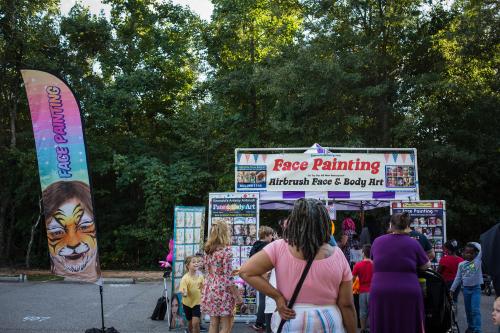 A vibrant face painting booth with colorful banners and children enjoying face art in a park setting.