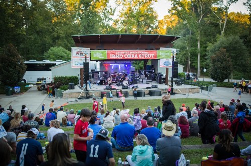 A lively outdoor concert scene with a crowd enjoying a performance on stage at the Irmo Okra Strut festival.