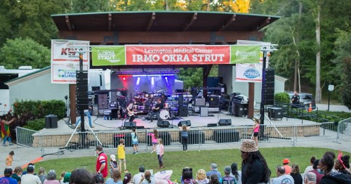 A lively outdoor concert scene with a stage, colorful lights, and an audience enjoying the performance at the Irmo Okra Strut.