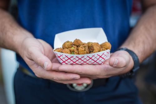 A person holds a tray of golden-brown, crispy fried food in a white container with a red checkered pattern.