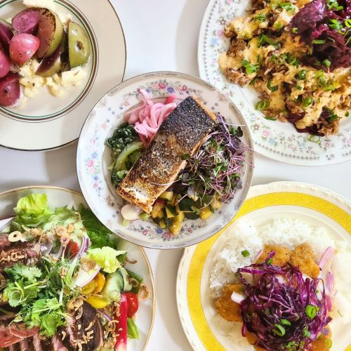 A colorful spread of dishes including salmon, salads, and sides, arranged on decorative plates.