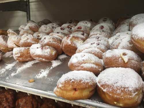 A tray of powdered sugar-covered donuts, some filled with fruit, arranged on a shelf in a bakery.