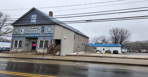 A two-story building with blue accents and a parking lot, set on a rainy day with bare trees in the background.