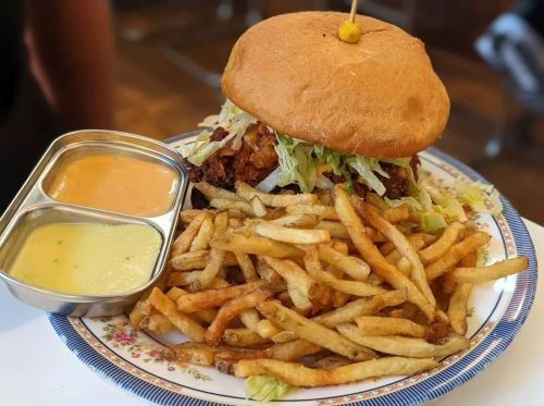 A plate with a large burger topped with lettuce and two dipping sauces, accompanied by a generous serving of fries.