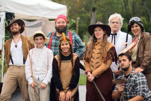 A group of people in costumes, including historical and adventurous themes, posing together outdoors.