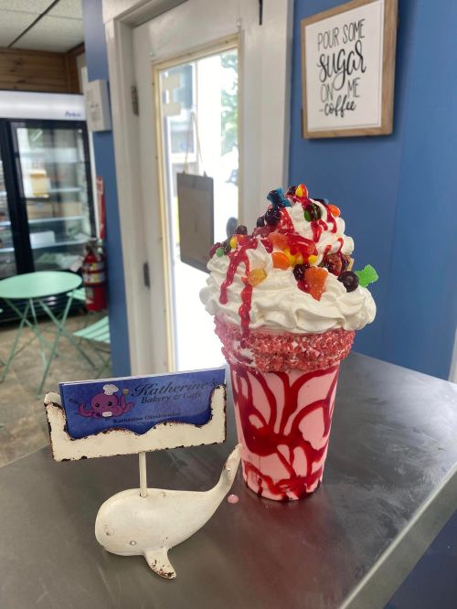 A colorful dessert topped with whipped cream and candy, served in a glass with a whale-shaped sign nearby.