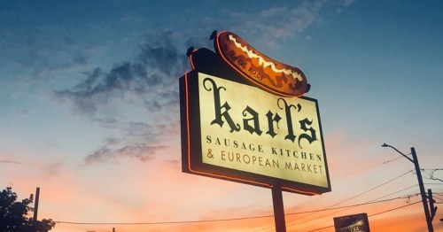 Sign for Karl's Sausage Kitchen & European Market against a colorful sunset sky.