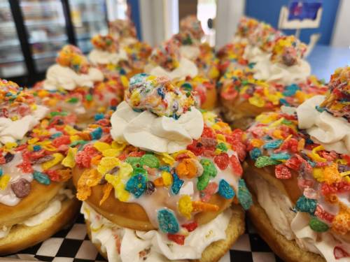 Colorful donuts topped with whipped cream and vibrant cereal sprinkles, arranged on a checkered paper.