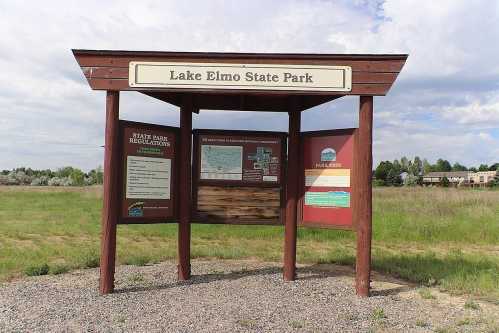 Sign at Lake Elmo State Park displaying park regulations and a map, set against a grassy field and cloudy sky.