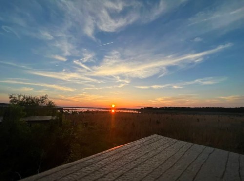 A serene sunset over a calm lake, with vibrant colors in the sky and silhouettes of trees in the foreground.