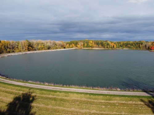 A serene lake surrounded by trees displaying autumn colors under a cloudy sky.