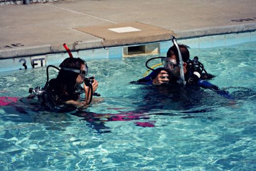 Two divers in scuba gear practice underwater skills in a swimming pool.