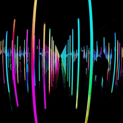 Colorful illuminated vertical lines create a vibrant, abstract tunnel effect with silhouettes of people in the foreground.