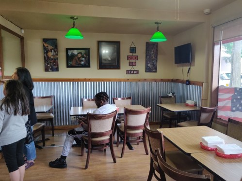 A casual restaurant interior with green lights, wooden tables, and a few patrons. An American flag is visible in the window.