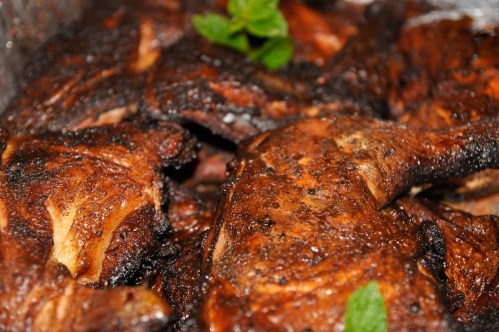 Close-up of grilled chicken pieces with a charred exterior, garnished with fresh mint leaves.
