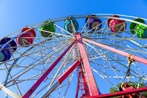A colorful ferris wheel against a clear blue sky, viewed from below, showcasing its vibrant passenger seats.