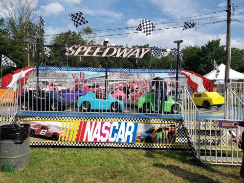Colorful go-karts on a small racetrack with NASCAR-themed decorations and checkered flags in the background.