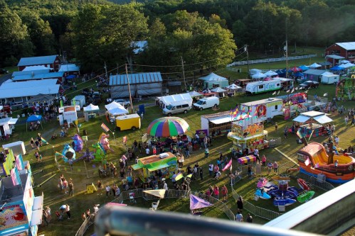 Aerial view of a vibrant fairground with colorful rides, food stalls, and crowds enjoying the festivities.
