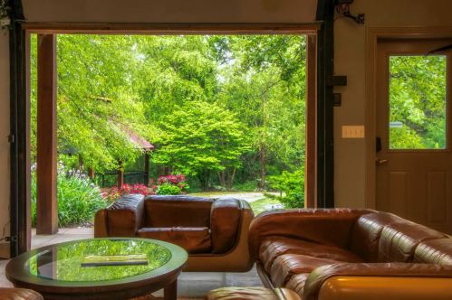 Cozy living room with leather sofas, open to a lush green garden through large sliding doors.