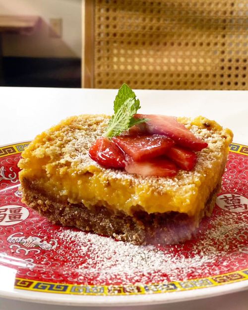 A slice of cheesecake topped with strawberries and mint, served on a decorative red plate.