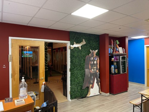 Interior of a colorful room with a green wall, a superhero cutout, and a snack area. Doors lead to another space.
