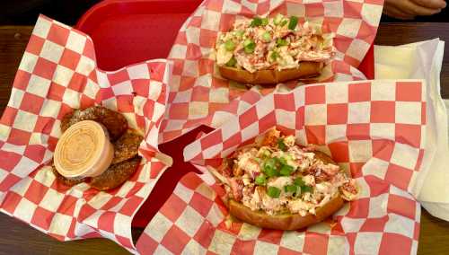 A red tray with two lobster rolls topped with green onions and a side of pretzel bites with dipping sauce.