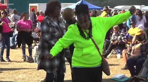 A lively outdoor event with people dancing and enjoying themselves in bright clothing and a festive atmosphere.
