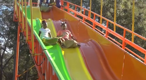 Children sliding down a colorful water slide, enjoying a sunny day at a water park.