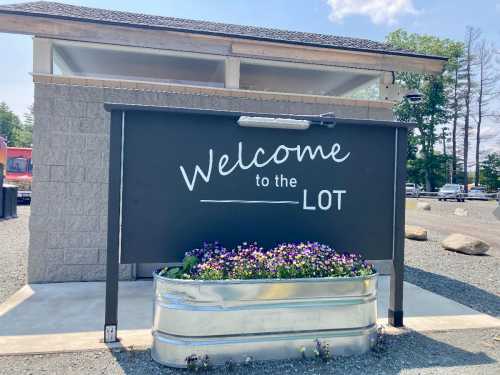 A sign reading "Welcome to the LOT" in front of a building, with a flower planter below it.