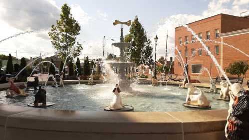 A decorative fountain with multiple water jets and animal sculptures around its edge, set in a sunny urban area.